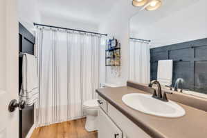 Bathroom featuring wood-finish flooring, a white vanity with dark hardware, a single basin sink with a dark bronze faucet, and a dark accent wall with board and batten detailing
