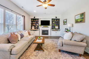 Living area featuring a ceiling fan, wood-finish flooring, and built-in shelving with integrated cabinetry