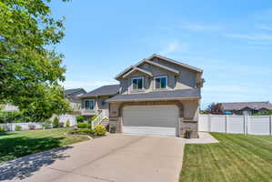Stucco exterior with brick accents, two-car garage, concrete driveway, and white picket fencing
