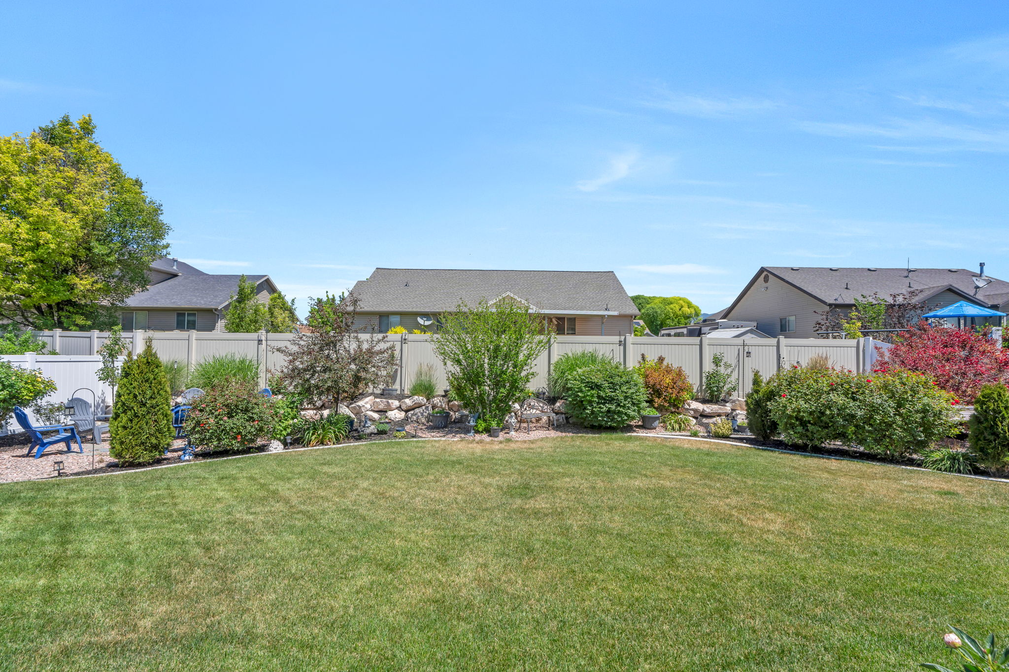Expansive backyard featuring a manicured lawn, established landscaping beds, and a perimeter fence