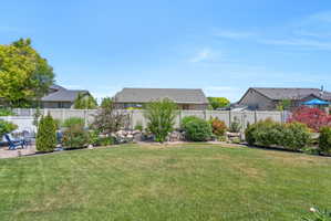Expansive backyard featuring a manicured lawn, established landscaping beds, and a perimeter fence