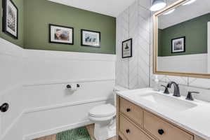 Powder room featuring a light wood-finish vanity with a built-in sink, dark bronze fixtures, a framed mirror, and a chevron tile accent wall