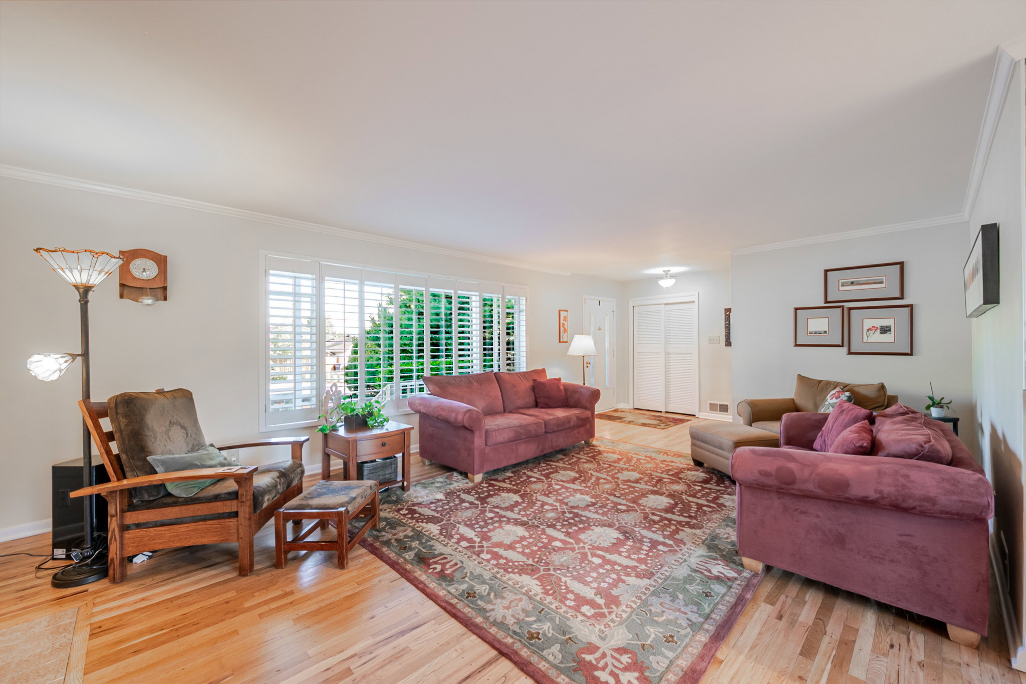 Spacious open living area featuring hard wood flooring, large windows with plantation shutters