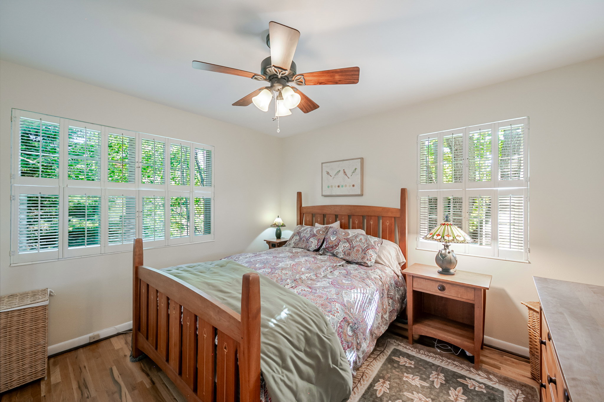 Large bright bedroom featuring multiple windows with white plantation shutters and hardwood floors
