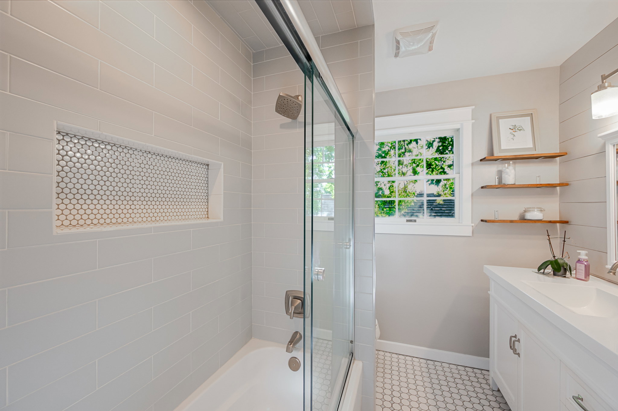 Newer Main Bathroom featuring a shower-tub combination with a glass sliding door, light gray subway tile surround, and a recessed niche with penny tile