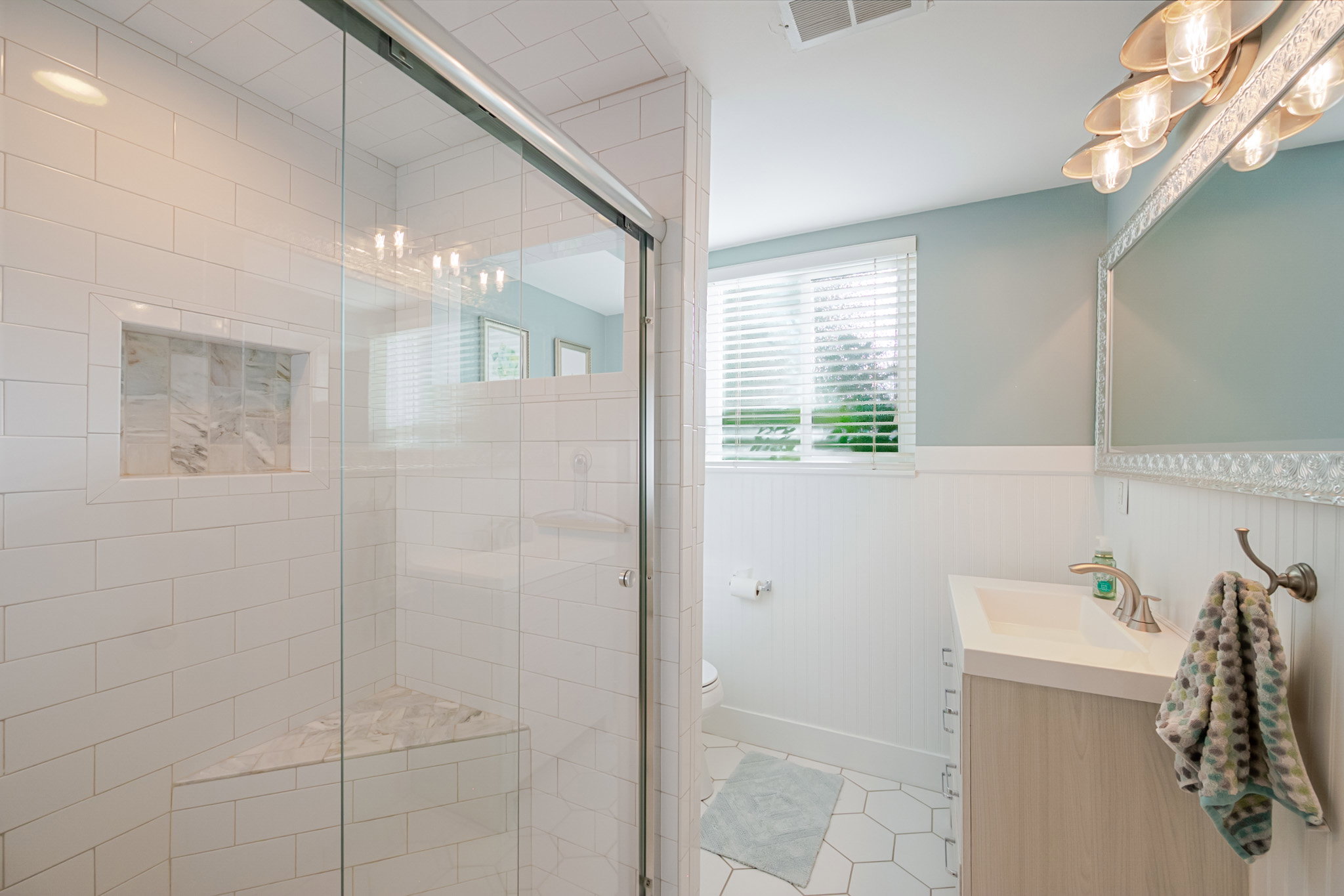 Bright new bath with custom Shower with sliding glass enclosure featuring white subway tile, a built-in bench, and a recessed niche