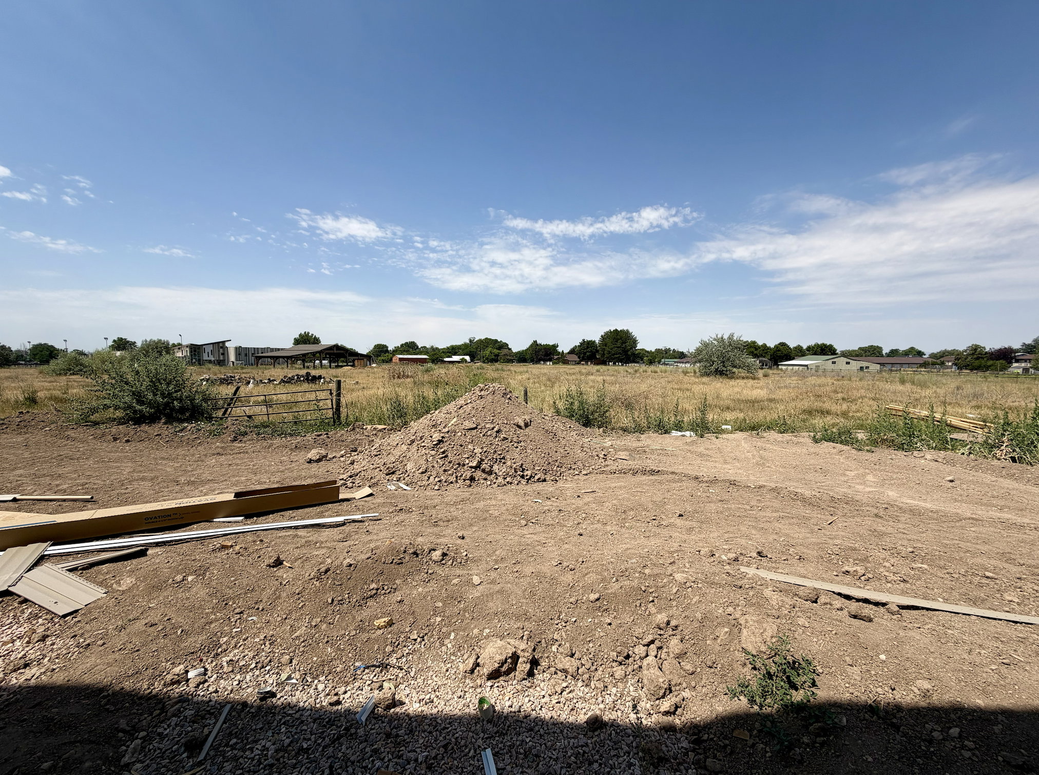 Expansive undeveloped lot featuring substantial earthwork, a partially fenced perimeter, and distant structures under a clear sky