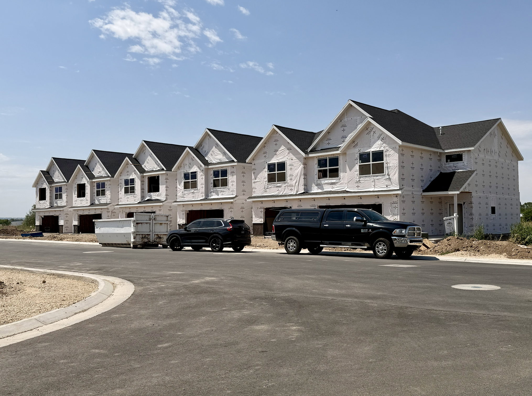 Row of newly constructed townhomes featuring dark shingle roofs and multiple gabled dormers