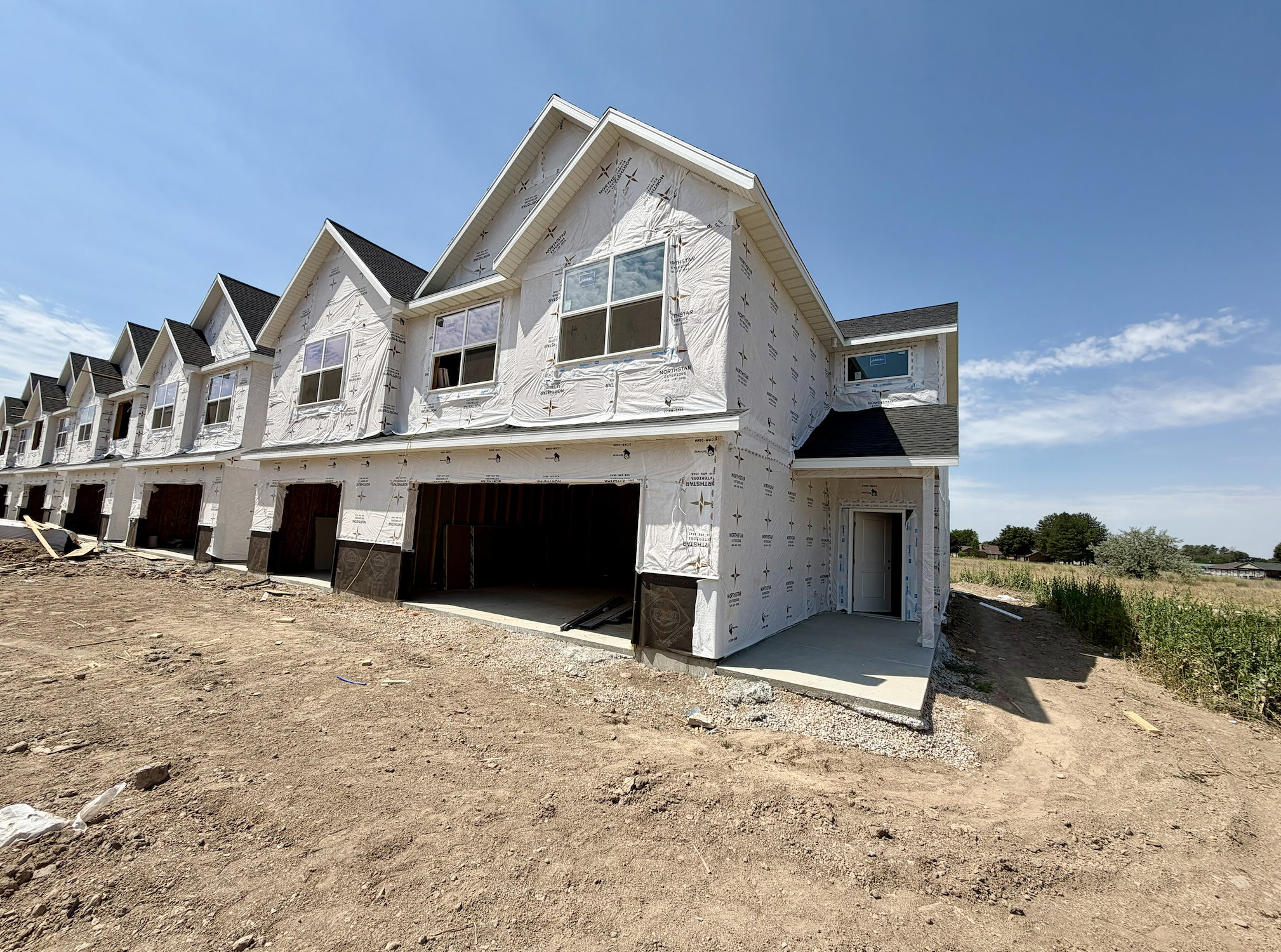 Townhouse row under construction featuring multiple gabled roofs, a prominent front entry with an overhang, and individual garage openings