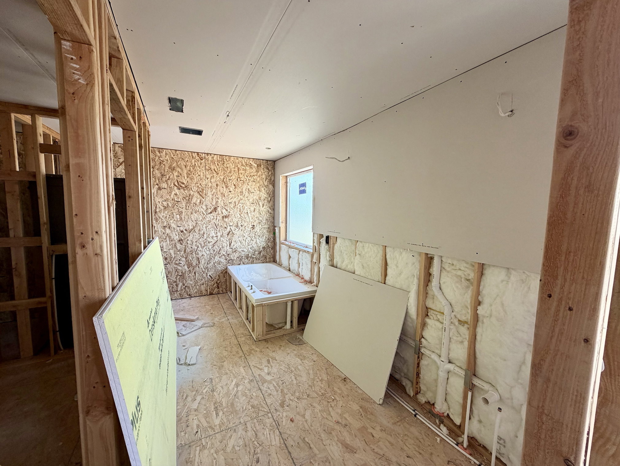 Interior space under construction featuring exposed wood framing, oriented strand board walls, and partial drywall installation