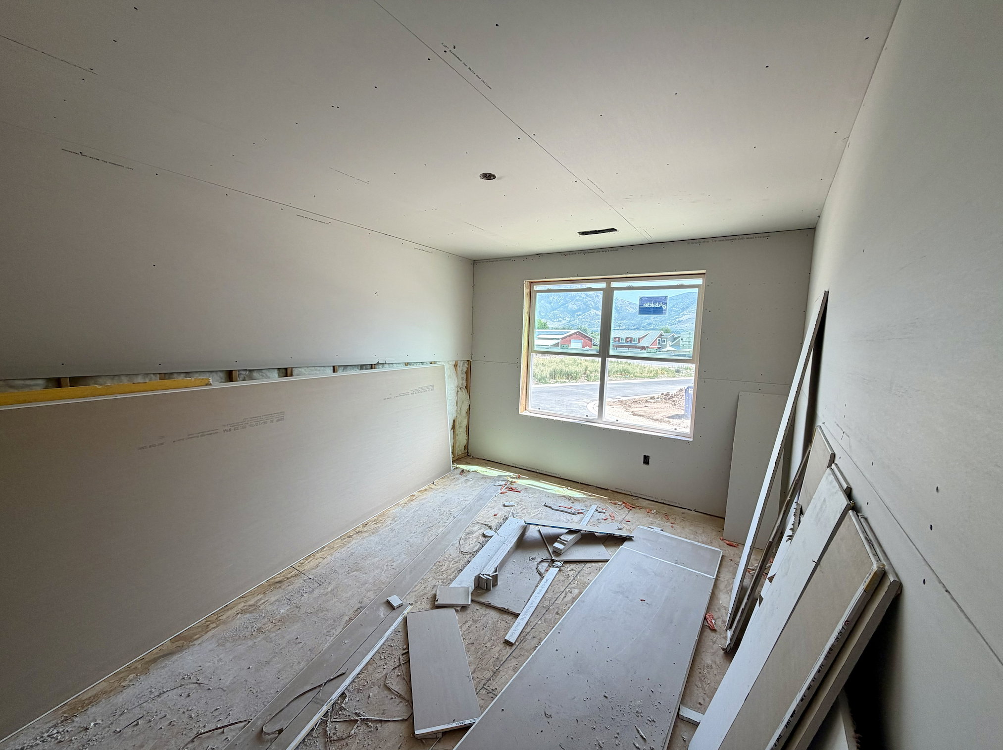 Room under construction featuring drywall installation, a large window, and an exposed subfloor