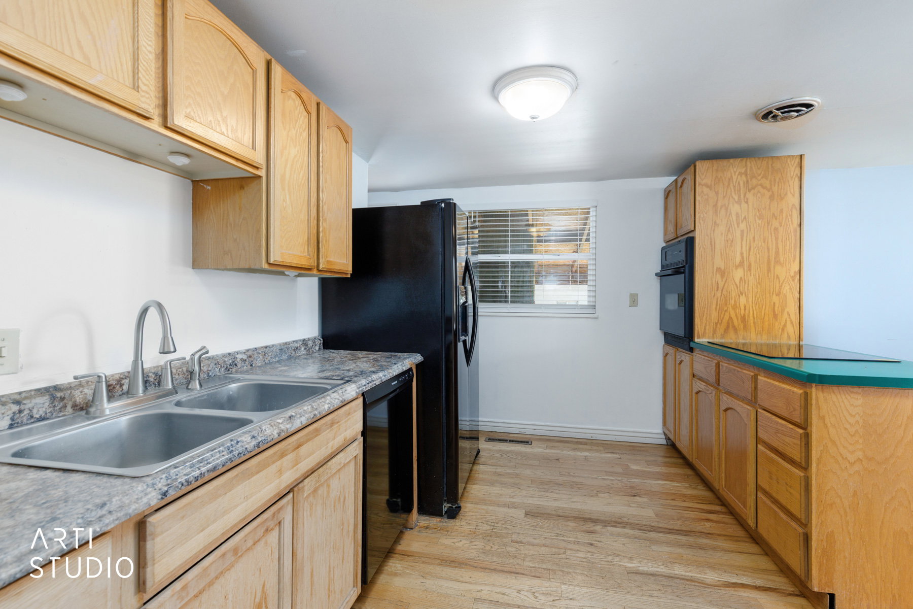 Kitchen space featuring wood-finish cabinetry, a double basin stainless steel sink with a brushed metal faucet, and black appliances including a refrigerator and built-in oven