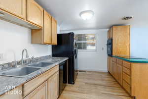Kitchen space featuring wood-finish cabinetry, a double basin stainless steel sink with a brushed metal faucet, and black appliances including a refrigerator and built-in oven