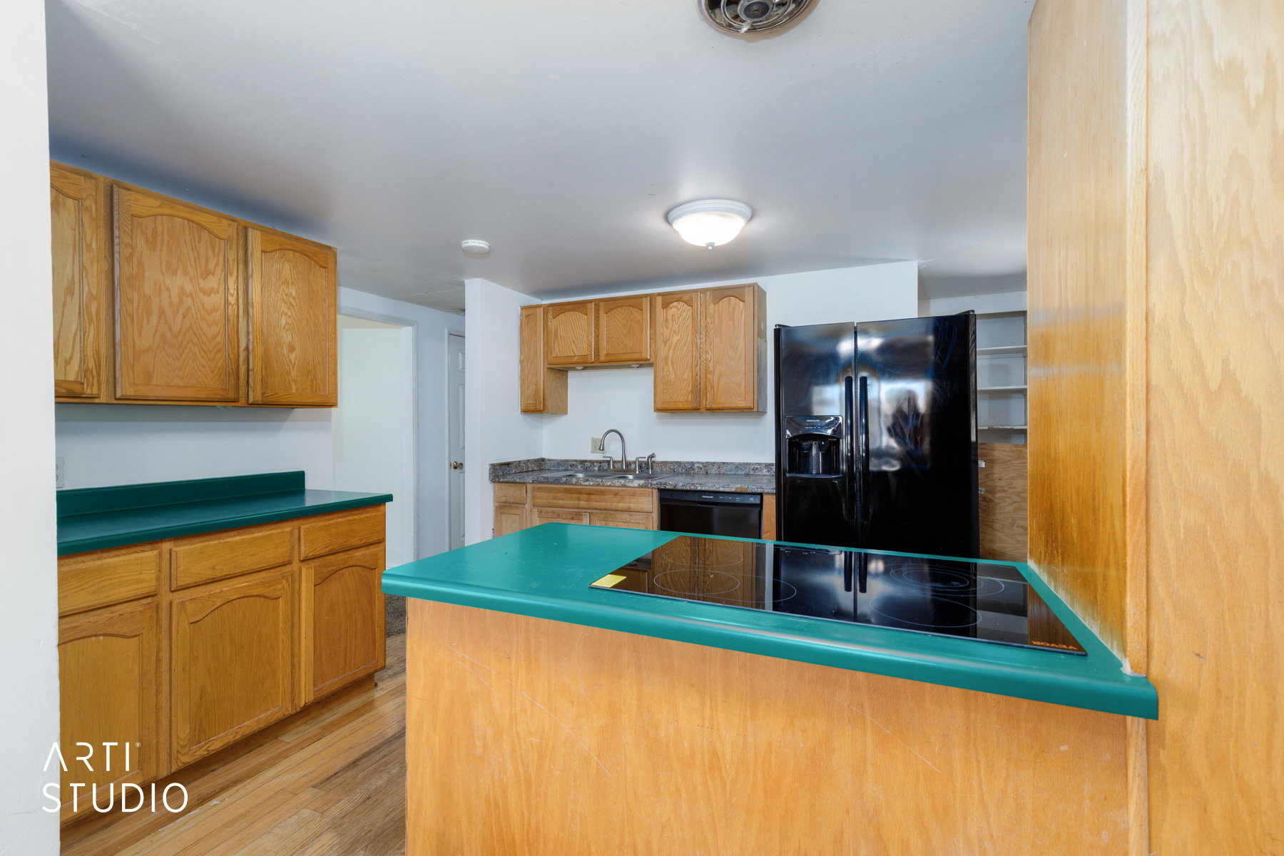 Kitchen featuring wood cabinetry, a black electric cooktop on an island, black refrigerator, and an undermount sink