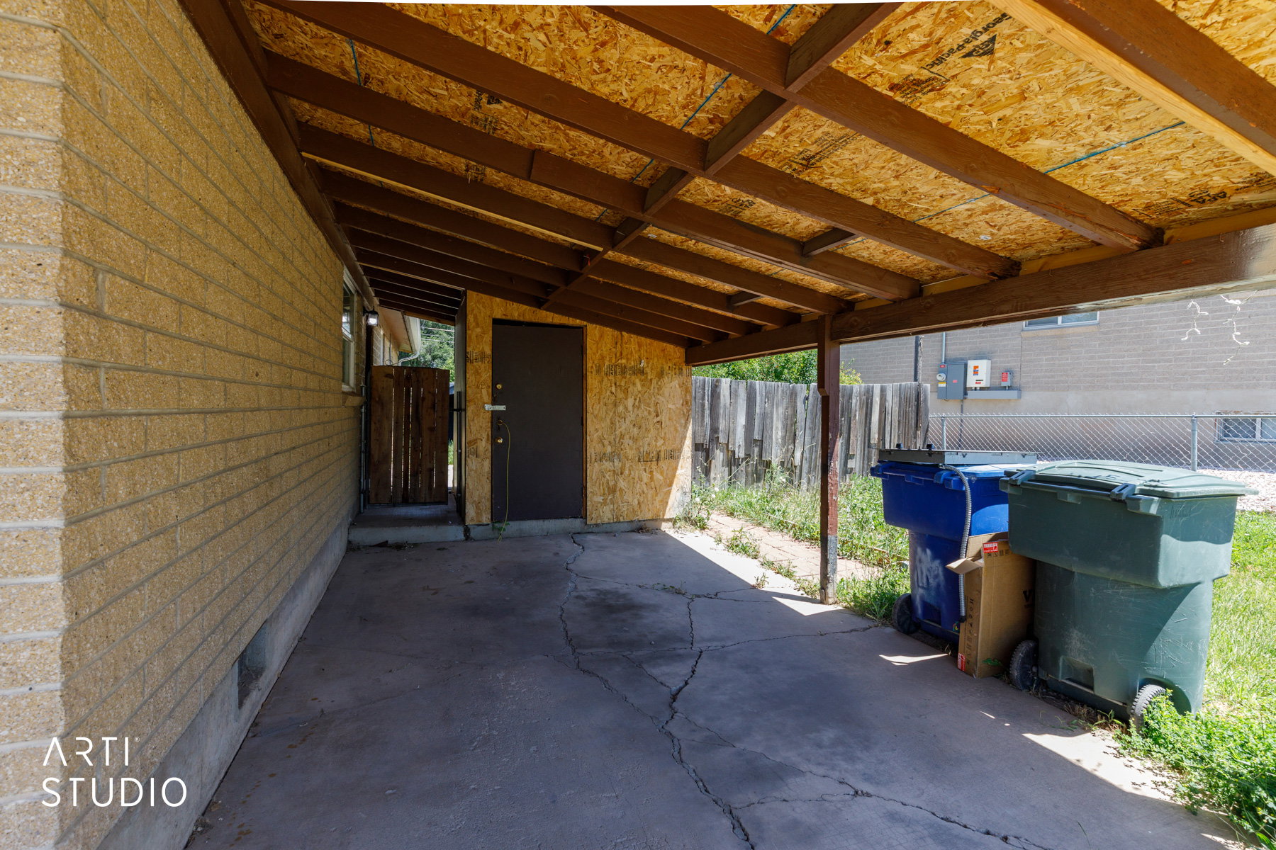 Carport structure with exposed wood beam ceiling, concrete flooring, and a side entrance door