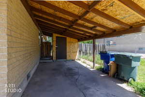 Carport structure with exposed wood beam ceiling, concrete flooring, and a side entrance door