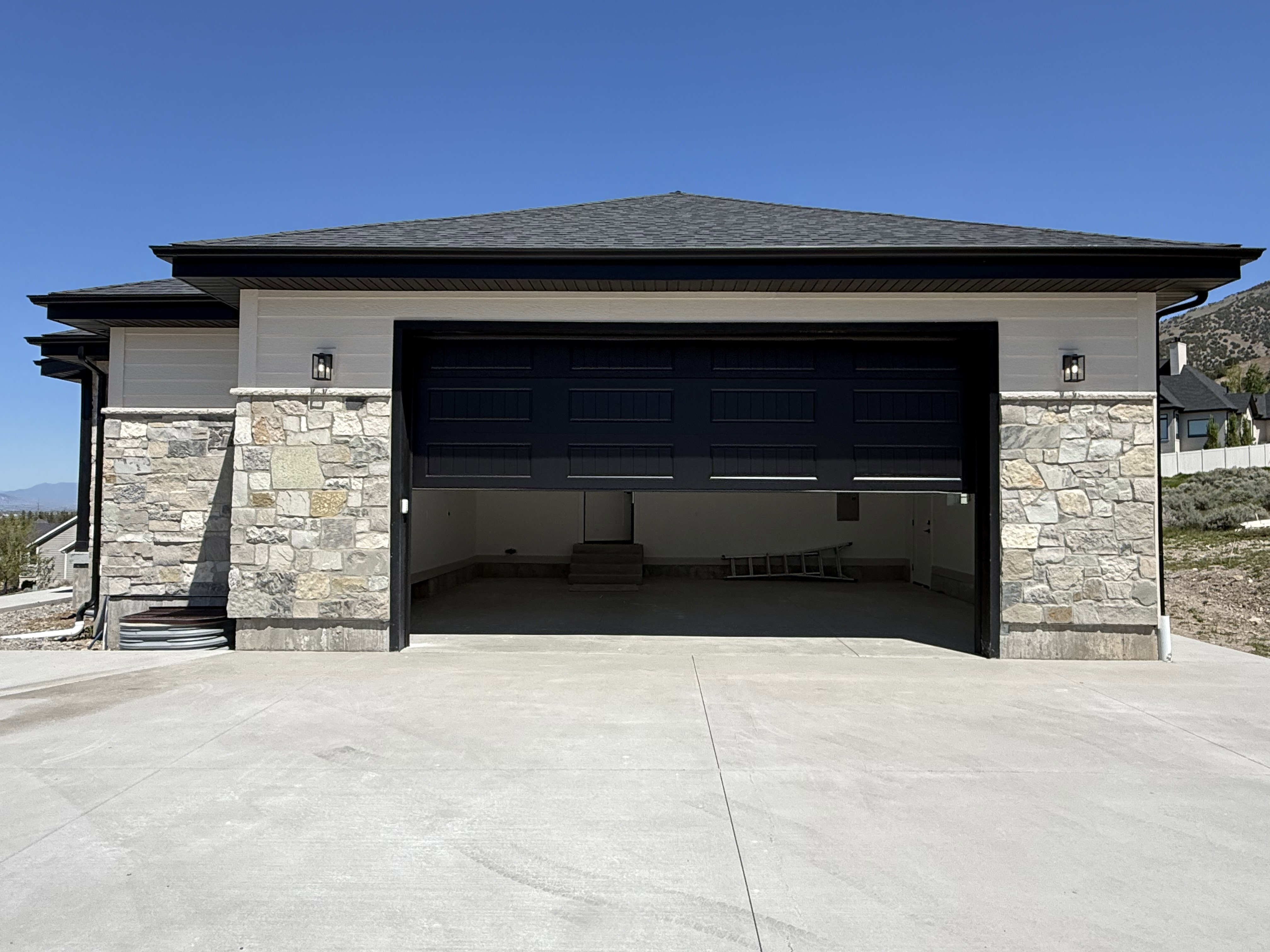Two-car garage featuring a dark paneled door, stone facade, and concrete driveway
