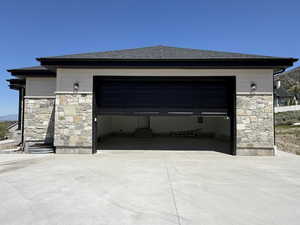 Two-car garage featuring a dark paneled door, stone facade, and concrete driveway