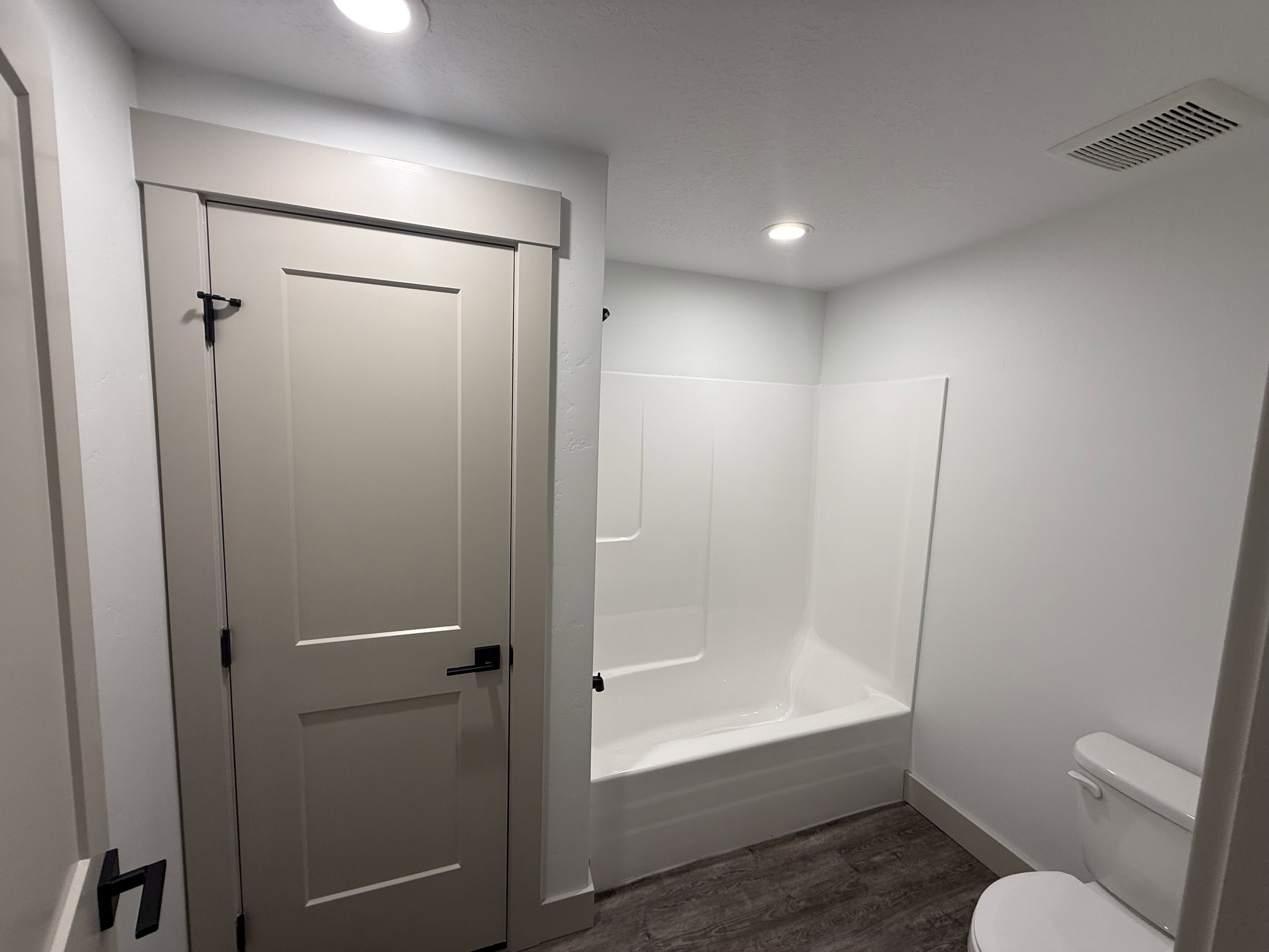 Bathroom featuring a white bathtub/shower combination, a toilet, wood-finish flooring, and recessed ceiling lighting