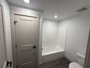 Bathroom featuring a white bathtub/shower combination, a toilet, wood-finish flooring, and recessed ceiling lighting