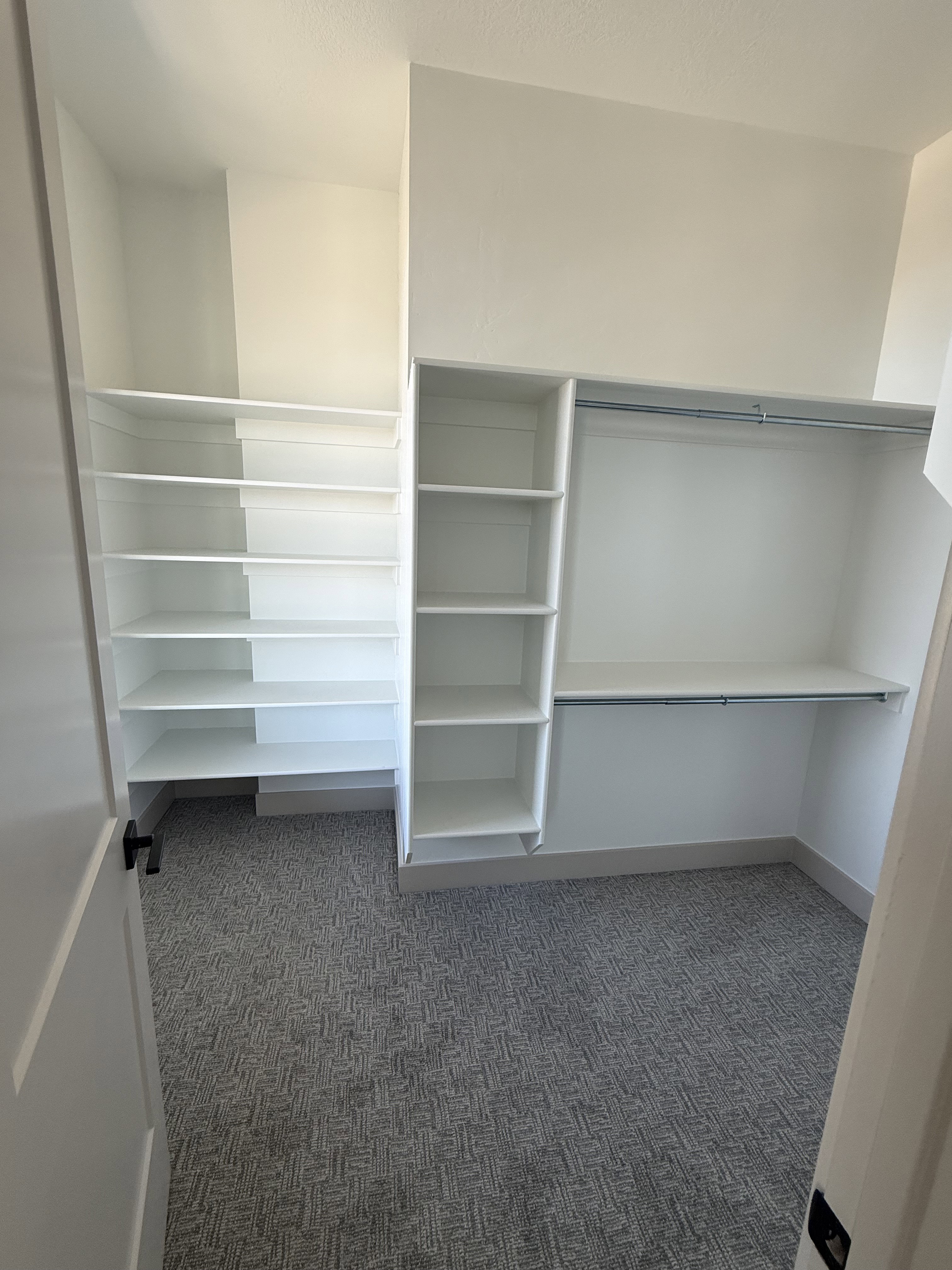 Built-in closet system featuring multiple shelves and hanging rods, complemented by patterned carpet flooring