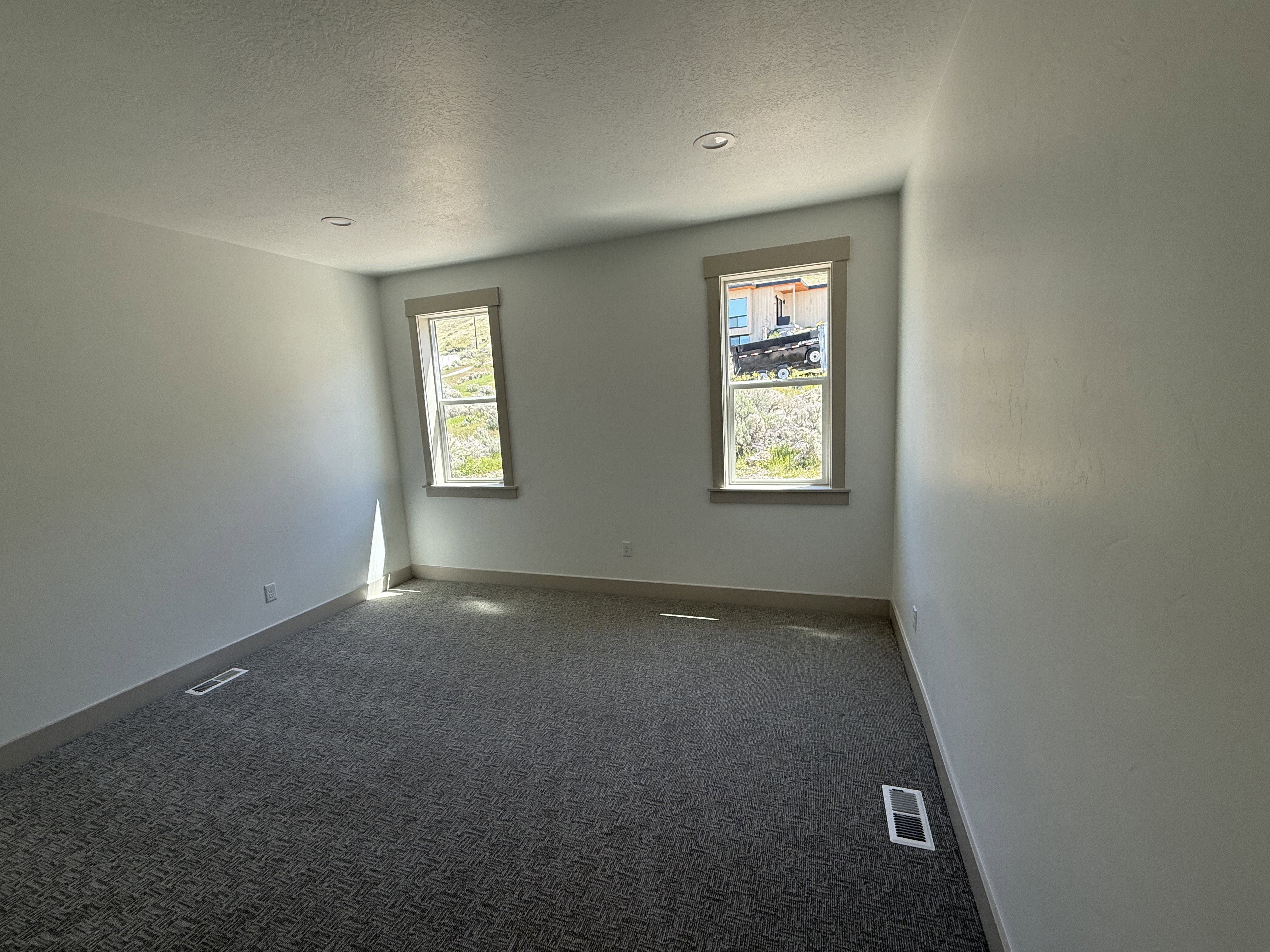 Spacious room featuring two windows with wood trim, recessed lighting, and patterned carpet flooring