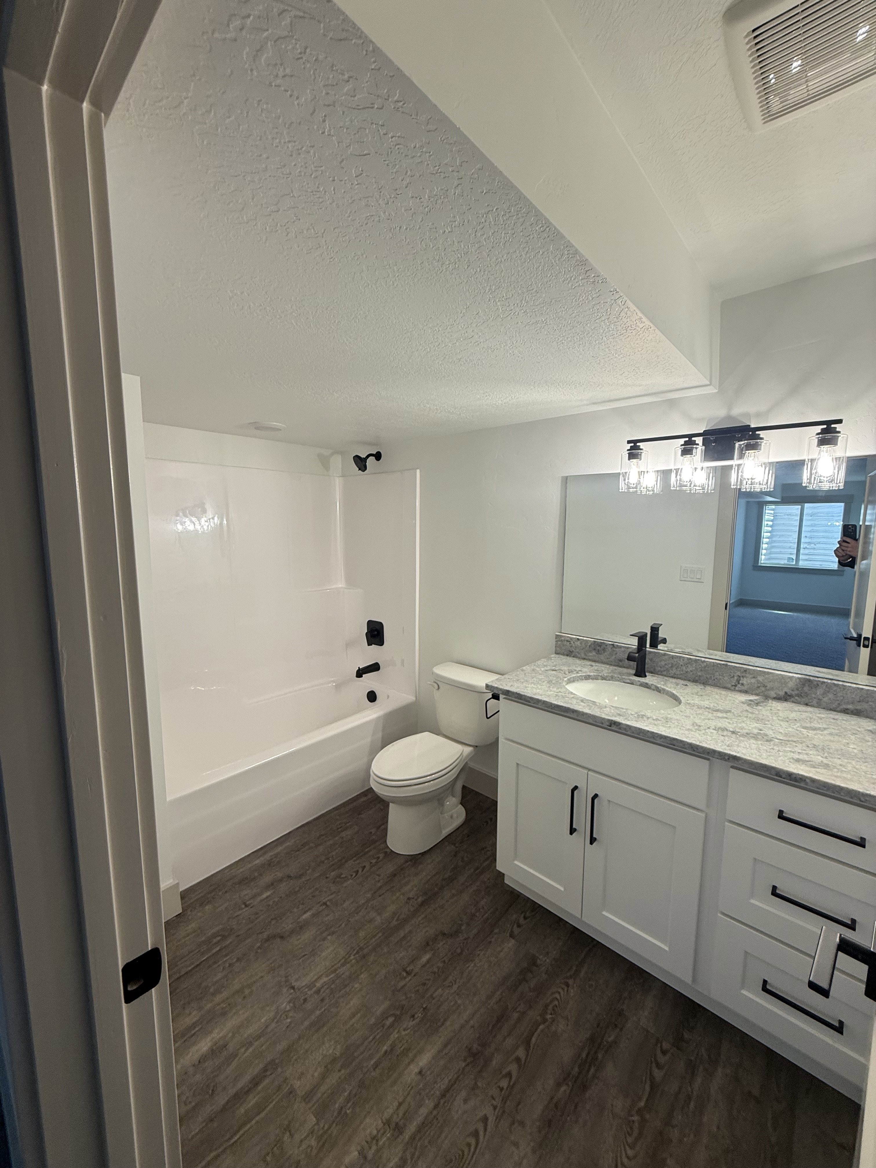 Bathroom featuring wood-finish flooring, a white vanity with shaker-style cabinetry, granite-finish countertop, and black hardware