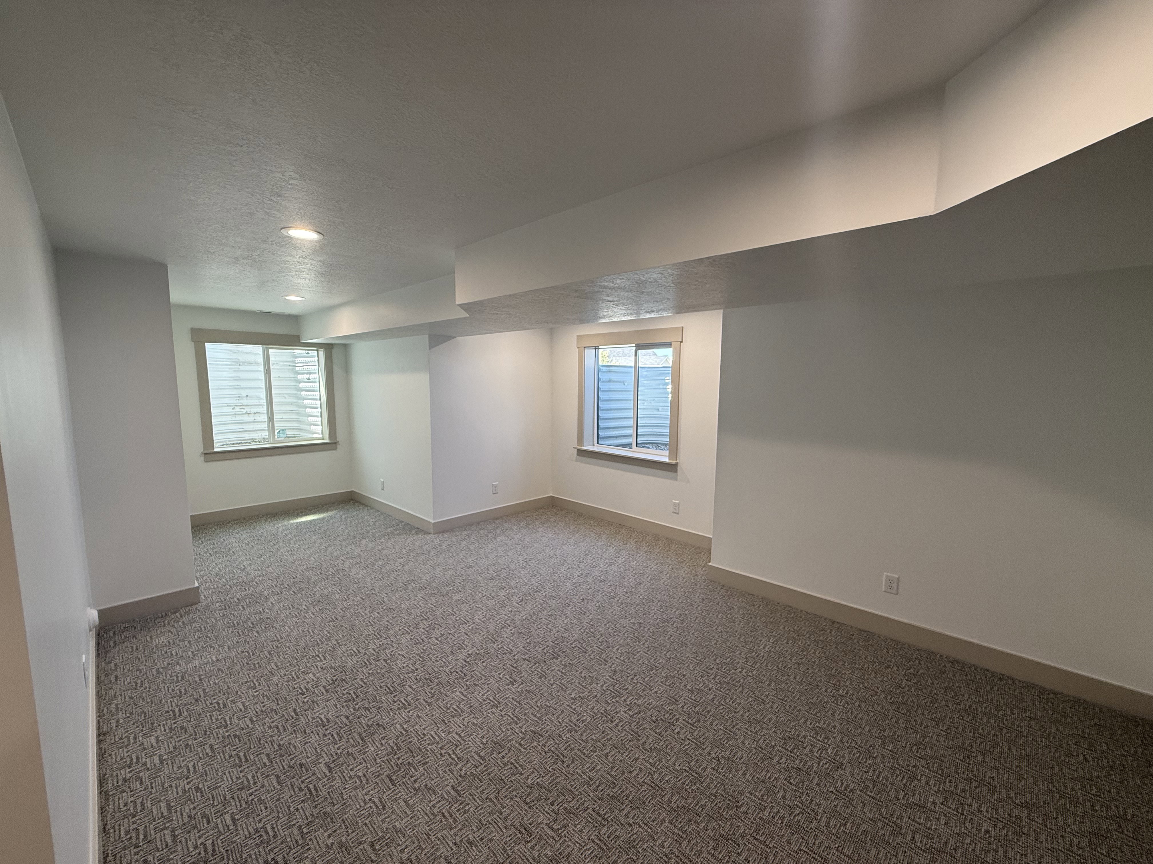 Spacious room featuring new patterned carpet, recessed lighting, two windows with wood-trim surrounds, and light-colored baseboards