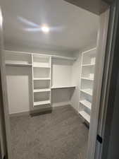 Walk-in closet featuring built-in white shelving, hanging rods, and patterned carpet flooring