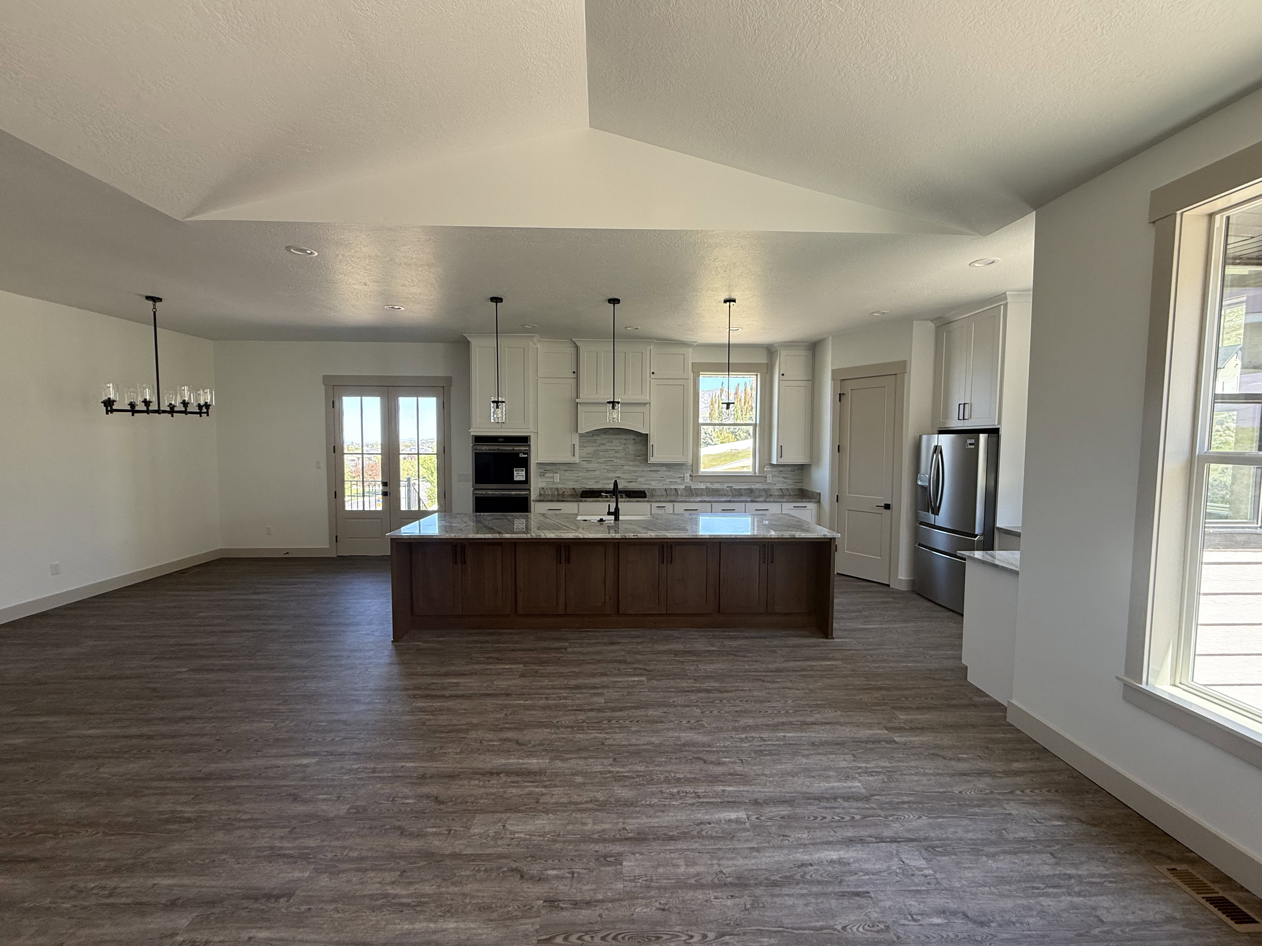 Spacious open-concept kitchen and living area featuring wood-finish flooring, white cabinetry, stainless steel appliances, a large central island with seating, and a double patio door