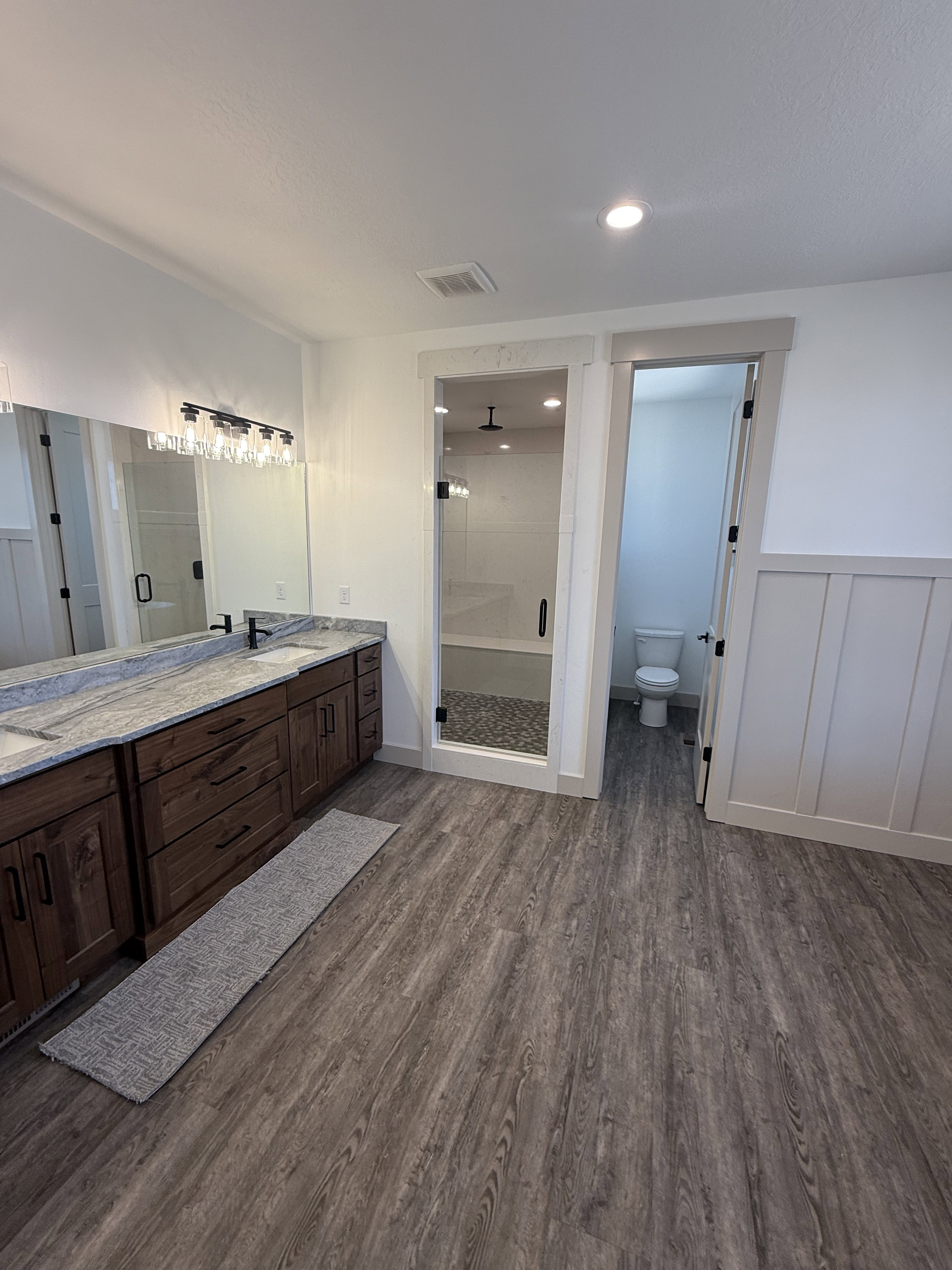 Bathroom featuring a dual vanity with a patterned countertop, rich wood-finish cabinetry, and a framed mirror