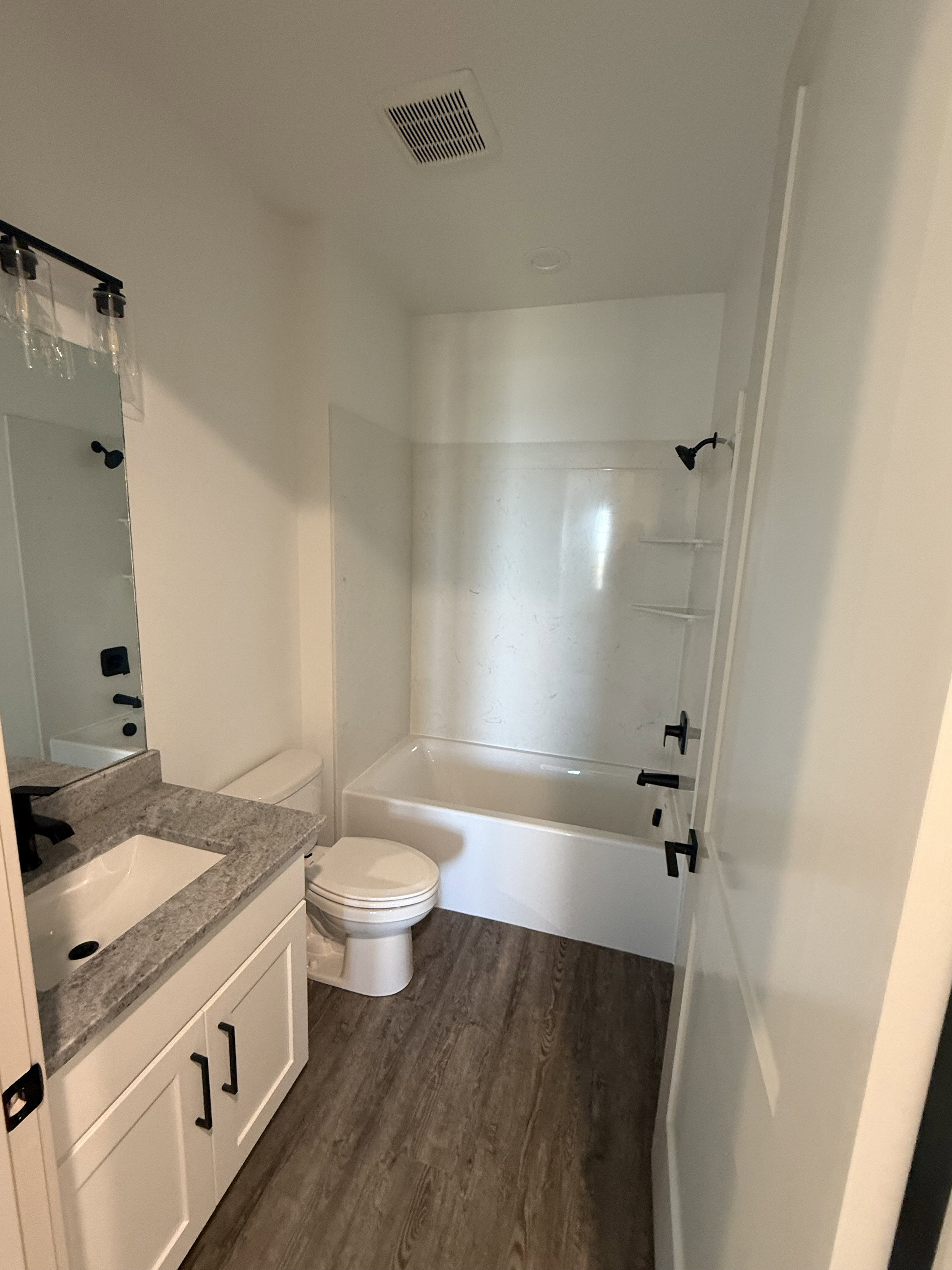 Bathroom with wood-finish flooring, white vanity with stone-finish countertop, and a white bathtub/shower combination