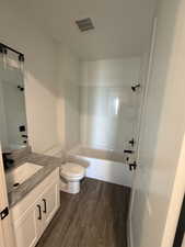 Bathroom with wood-finish flooring, white vanity with stone-finish countertop, and a white bathtub/shower combination