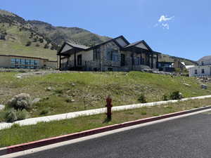 Modern mountain home featuring stone and siding exterior, large windows, an expansive covered porch with dark railings, and a hillside setting