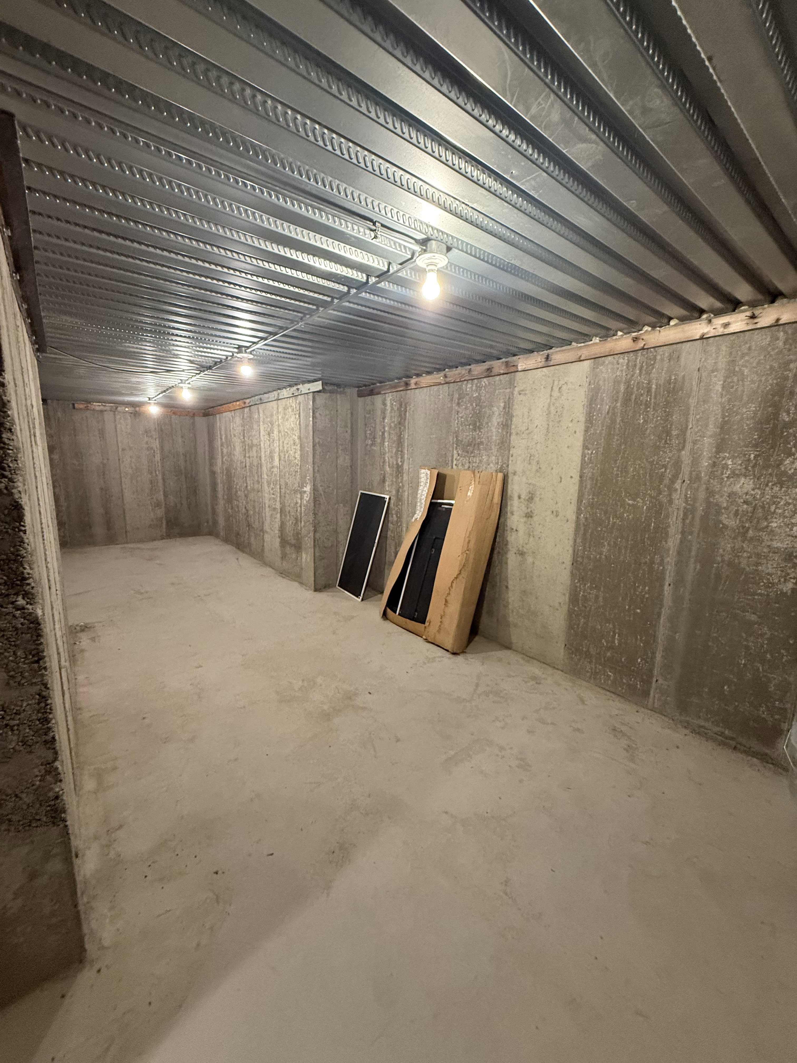 Unfinished basement featuring concrete walls, a concrete floor, and a metal ceiling with exposed lighting fixtures