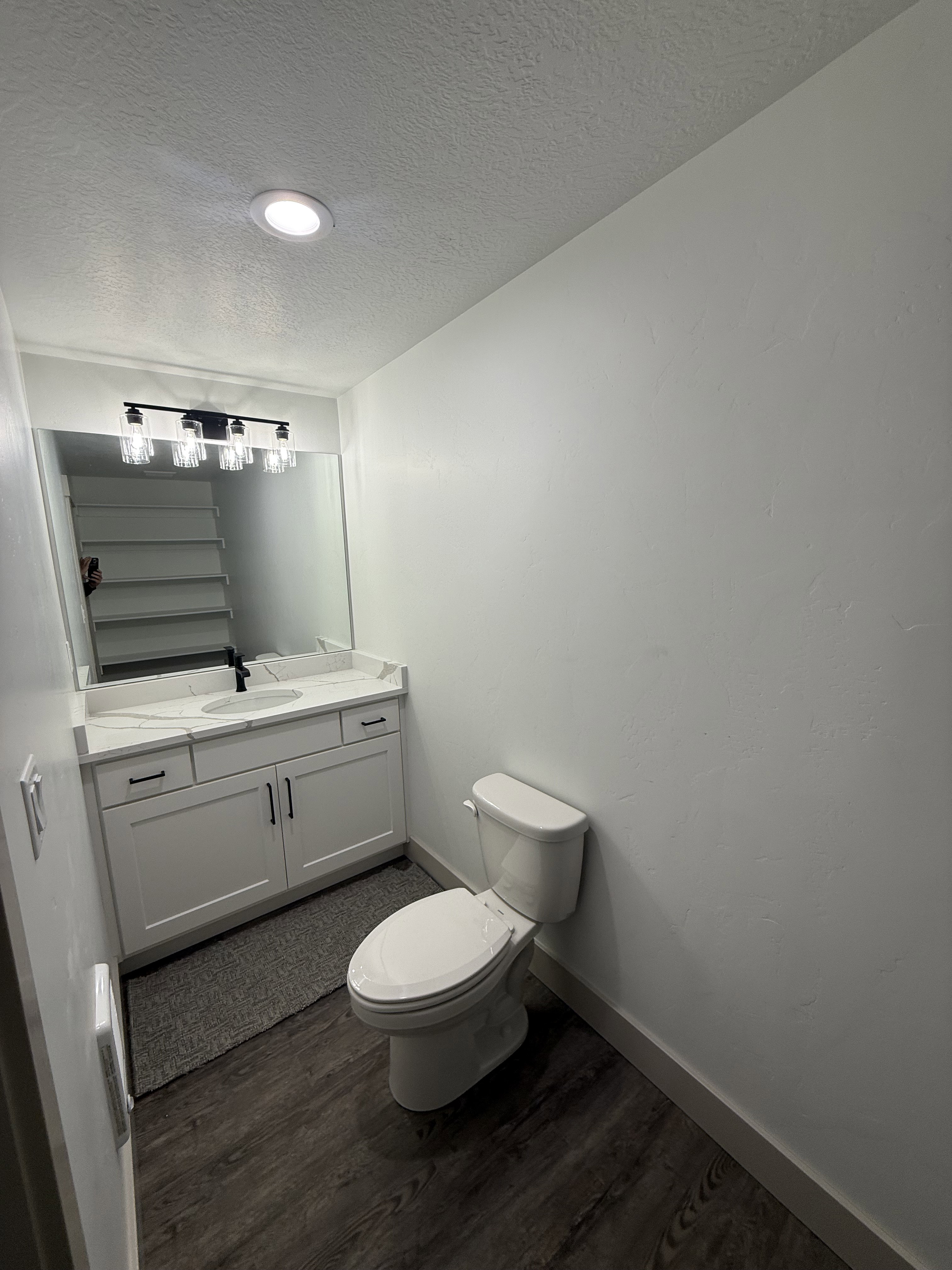 Bathroom featuring a dual-sink vanity with white cabinetry, a light-toned countertop, and dark wood-finish flooring