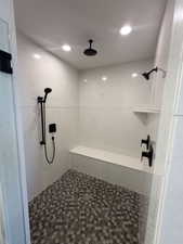 Spacious walk-in shower featuring a rain shower head, additional shower head with handheld sprayer, matte black fixtures, built-in bench, and hexagonal mosaic tile flooring