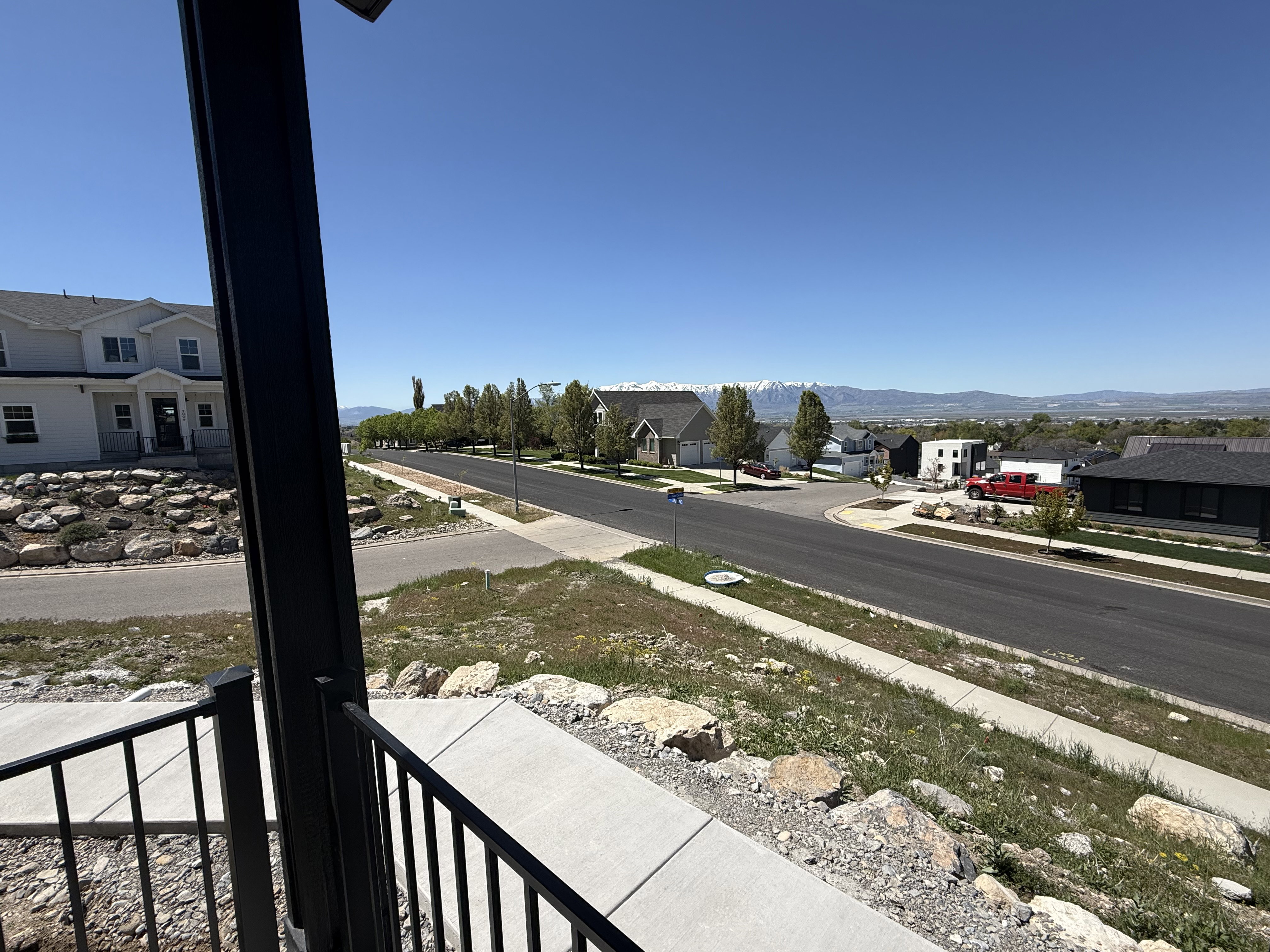 Exterior porch with black metal railing, featuring a concrete walkway and landscaping with natural rock elements