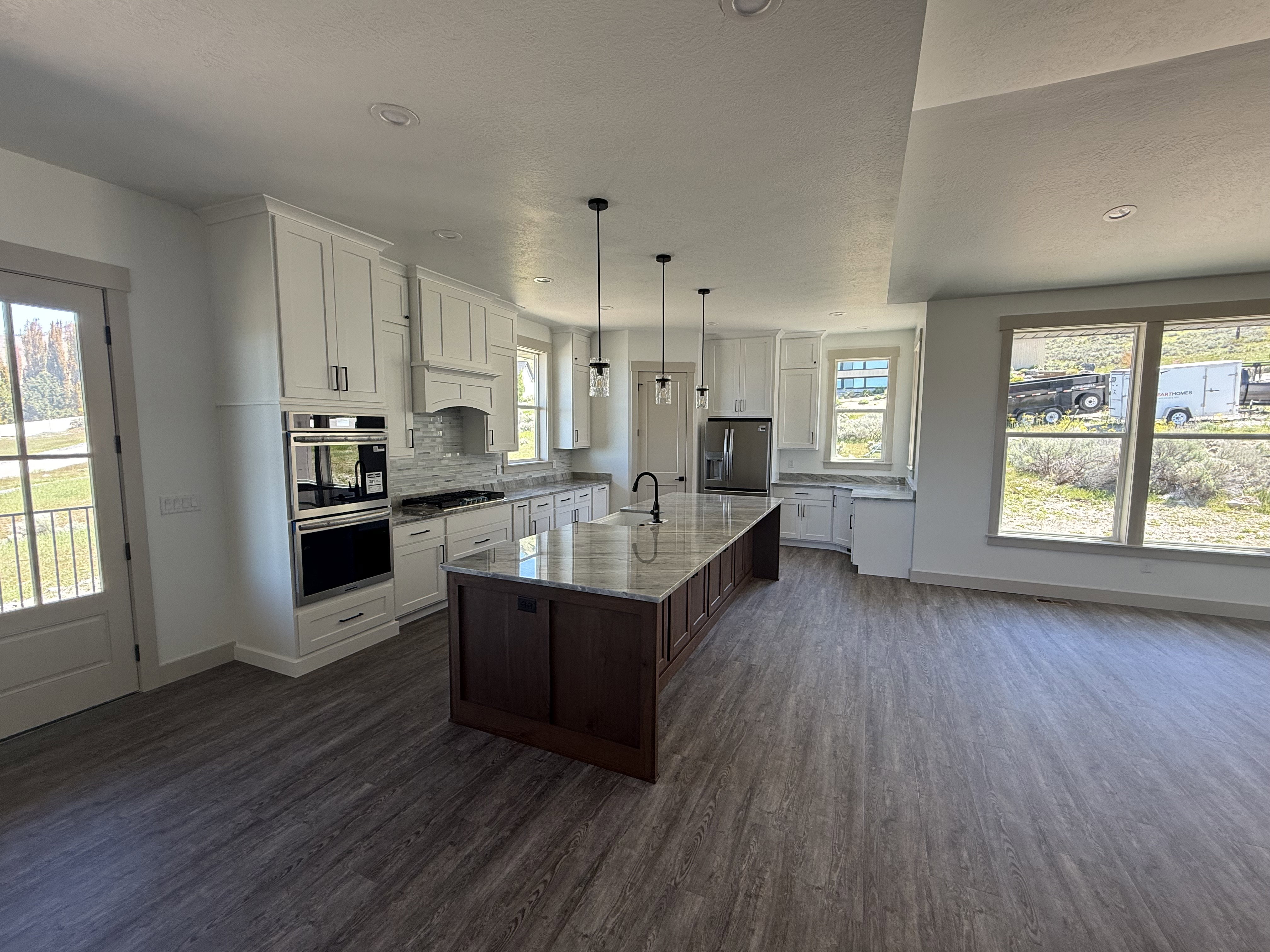 Open-concept kitchen featuring a large central island with a wood base and stone countertop, white upper and lower cabinetry, stainless steel appliances, and wood-finish flooring