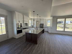 Open-concept kitchen featuring a large central island with a wood base and stone countertop, white upper and lower cabinetry, stainless steel appliances, and wood-finish flooring