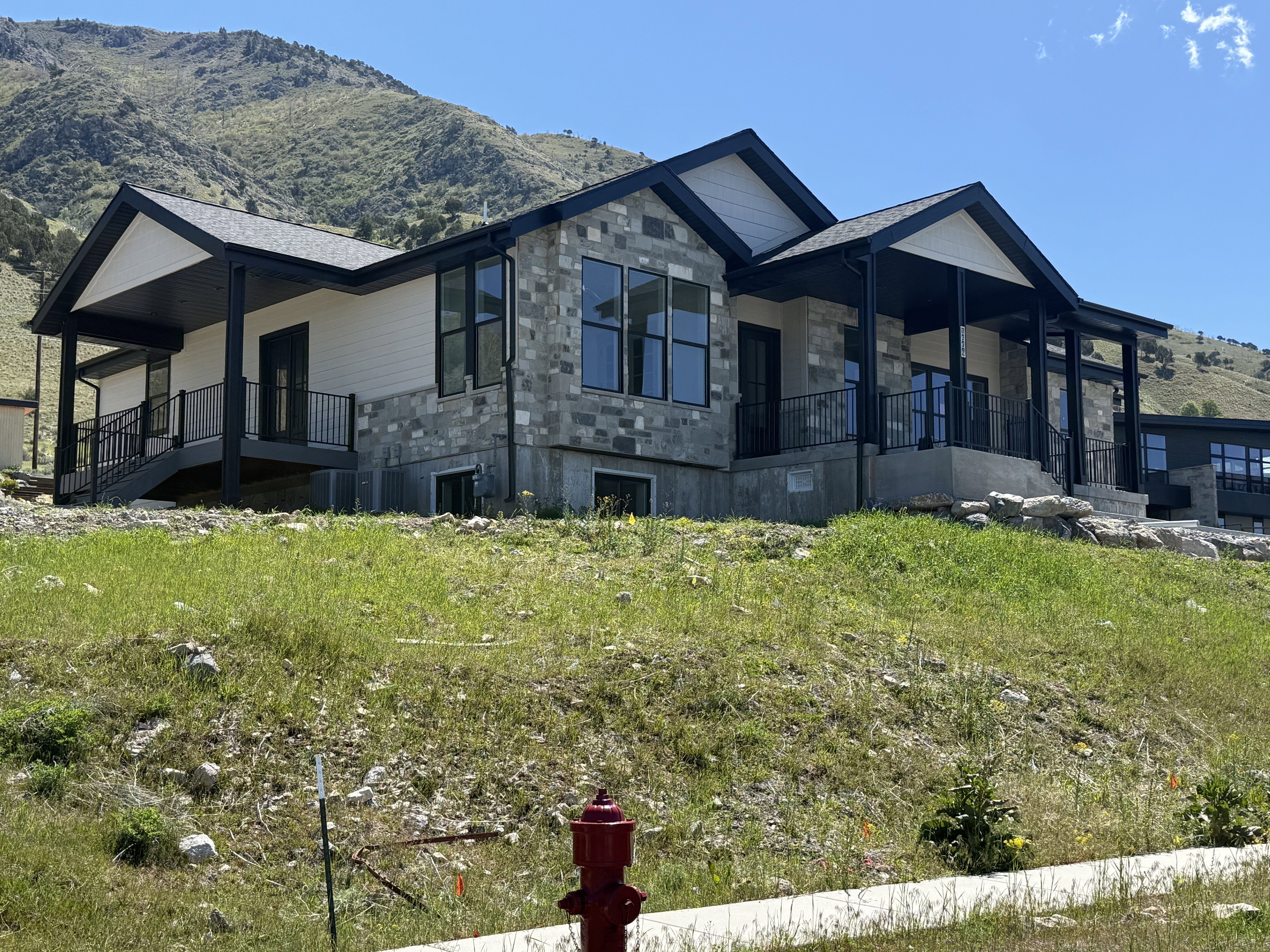 Modern residence featuring a stone and siding exterior, multiple covered patios, black-framed windows, and a black shingle roof