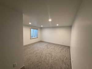 Spacious room featuring neutral carpeting, recessed ceiling lighting, and a window with white trim