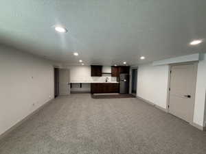 Spacious room featuring recessed lighting, a built-in kitchenette with dark wood-finish cabinetry, a stainless steel refrigerator, and a white countertop with an undermount sink