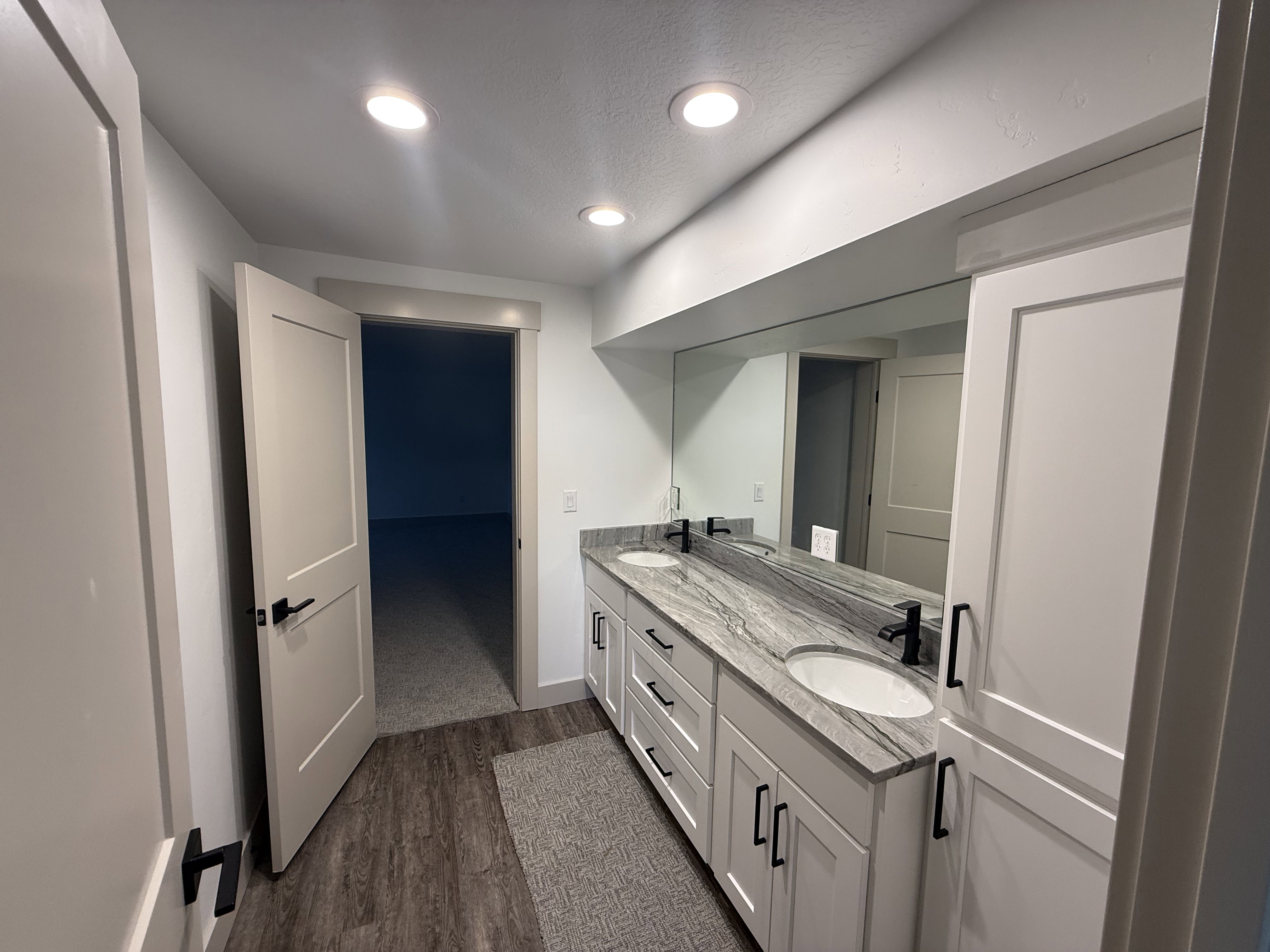 Double vanity featuring white shaker cabinetry, an integrated mirror, and a stone countertop with dual undermount sinks and matte black fixtures
