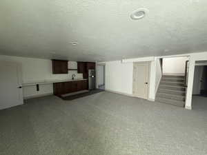 Spacious lower-level area featuring a kitchenette with dark wood cabinetry, a stainless steel refrigerator, and a sink with a matte black faucet