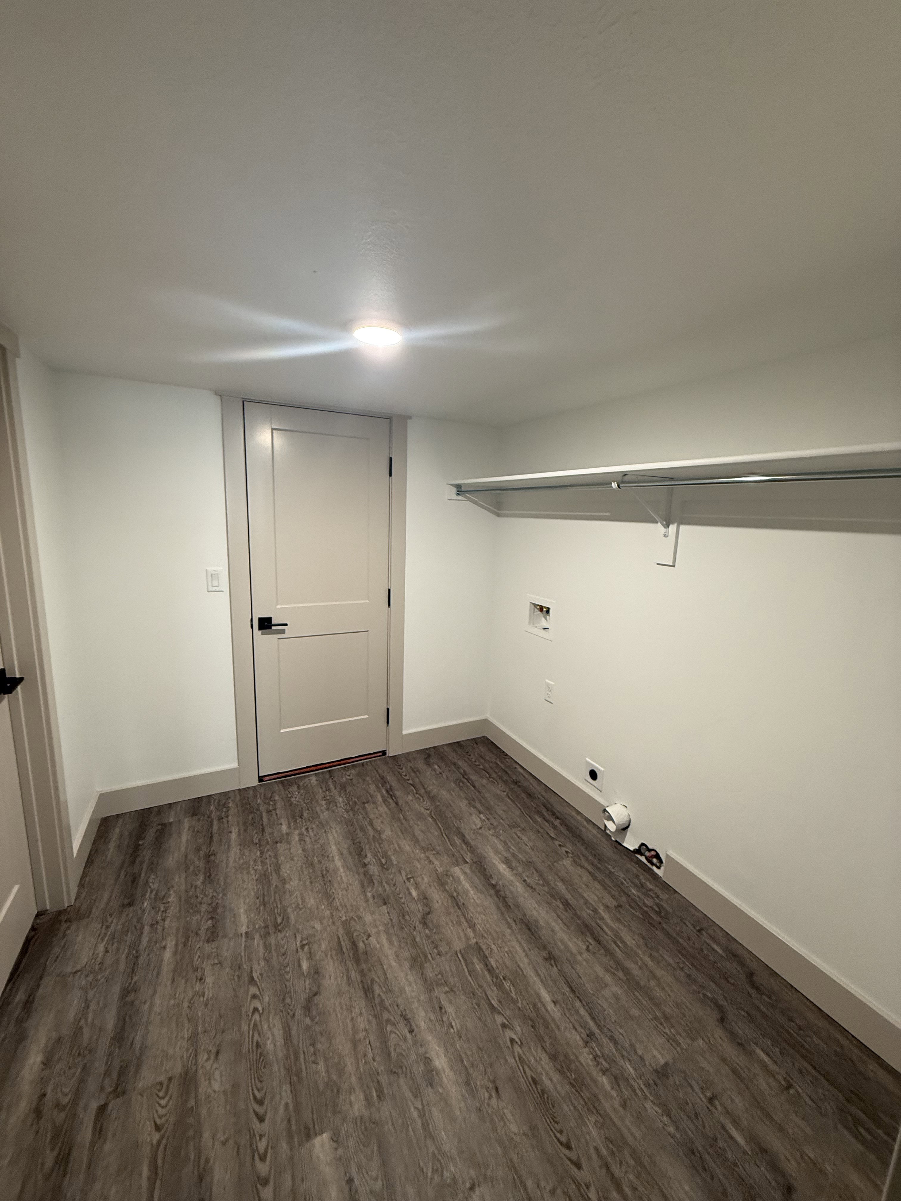 Dedicated laundry area with wood-finish flooring, white walls, and a built-in wire shelf