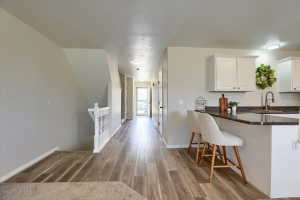 Open-concept living space featuring wood-finish flooring, white cabinetry, a built-in kitchen island with seating, and recessed ceiling lighting