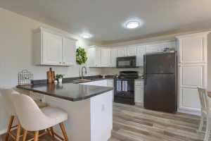Kitchen featuring white shaker-style cabinetry, dark countertops, black appliances, and wood-finish flooring