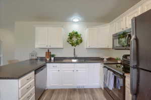 Kitchen featuring wood-finish flooring, white cabinetry, dark countertops, a stainless steel dishwasher, and black appliances including a range and microwave