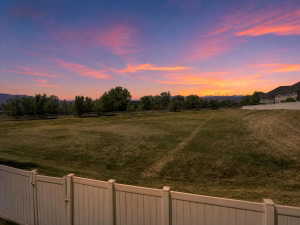 Expansive grassy lot bordered by a white privacy fence and a natural tree line, with a mountain backdrop
